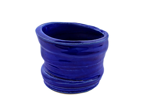 Dark blue ceramic cup isolate. Glass glossy decorative close-up. Pot with jagged edges made of blue-glazed clay.