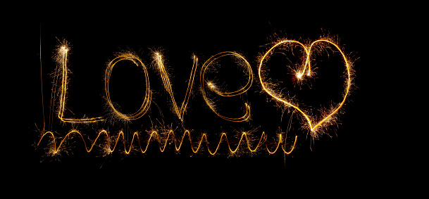 Inscription Love and heart of sparklers. Sparks of holiday lights on black background with heart and spiral