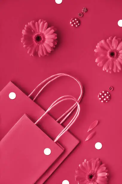 Viva Magenta color of the year 2023. Gerbera daisy flowers and craft papper shopping bags, flat lay, top view from above. Monochromatic red springtime background.