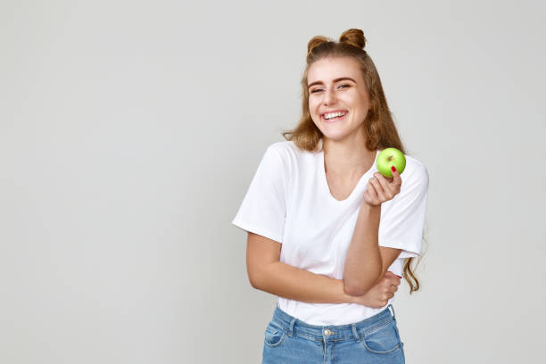 ragazza che tiene la mela verde sullo sfondo dello studio - apple women green eating foto e immagini stock