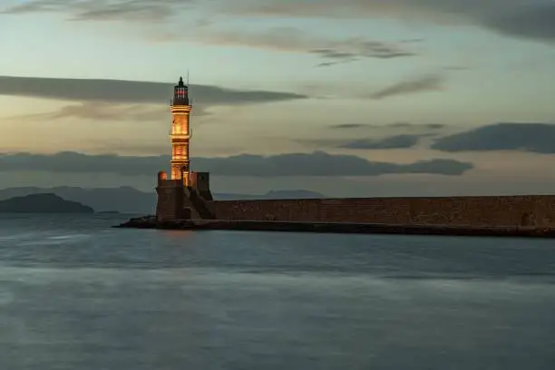 Photo of Lighthouse in the center of a sea beneath the clouded sky of Greece's sunset