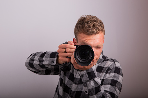 Portrait of a photographer taking a picture with his camera, studio shot with white background