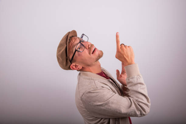 Stylish man wearing flat cap points up with surprised expression, advertising photography with copy space