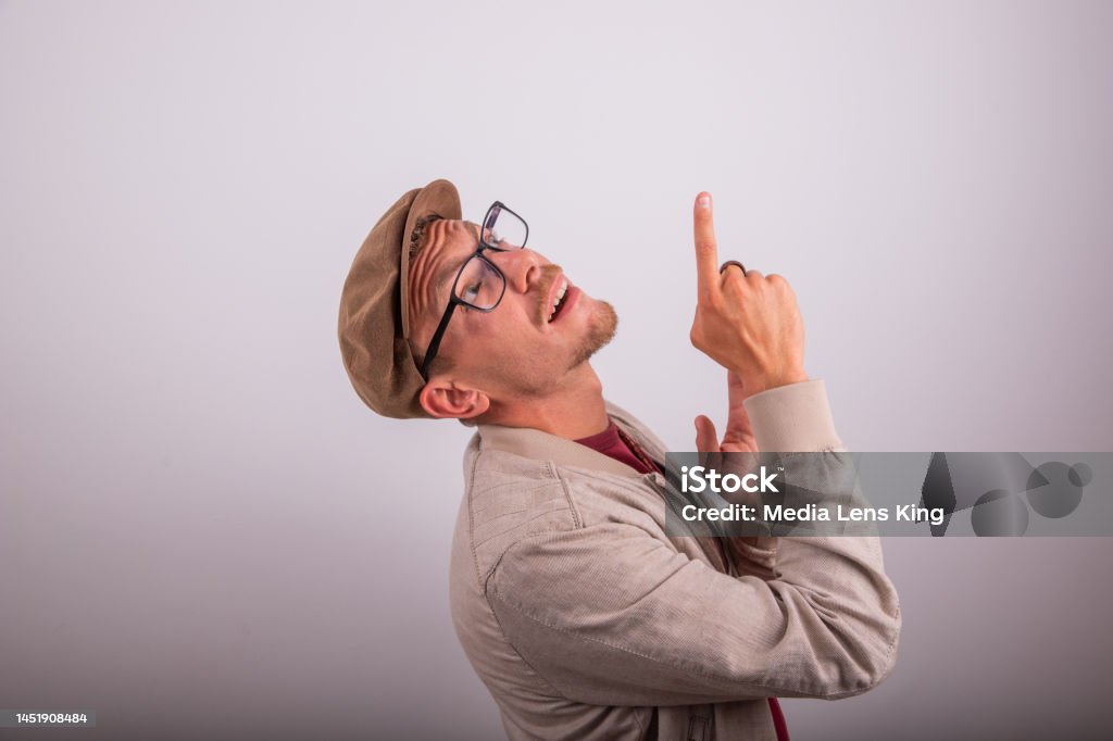 Stylish man wearing flat cap points up with surprised expression, advertising photography with copy space. Stylish man wearing flat cap points up with surprised expression, advertising photography with copy space 20-29 Years Stock Photo