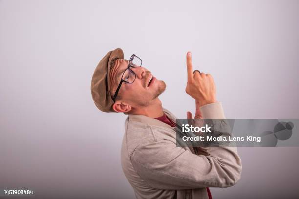 Stylish Man Wearing Flat Cap Points Up With Surprised Expression Advertising Photography With Copy Space Stock Photo - Download Image Now