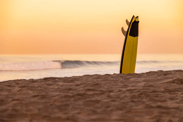 Yellow Surfboard Upside Down in the Sand at Sunset This is a photo of a yellow surfboard stuck in the sand on the beach by the ocean waves at the golden hour of sunset surf boards stock pictures, royalty-free photos & images
