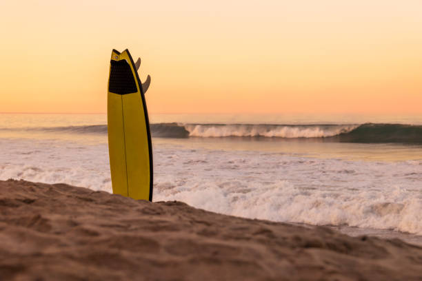 Yellow Surfboard Upside Down in the Sand at Sunset stock photo