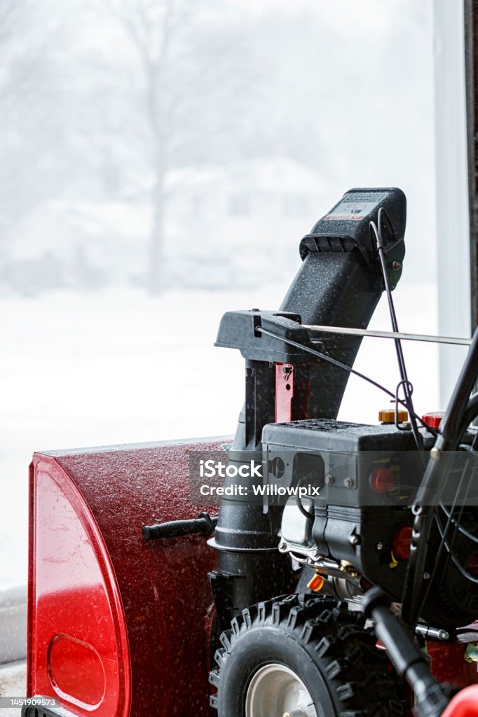 DIY Home Owner Snow Blower Ready for Blizzard Snow DIY residential homeowner's gasoline powered snow blower is waiting at the open garage doorway ready to get started clearing deep winter blizzard snow from the home driveway. Winter Stock Photo
