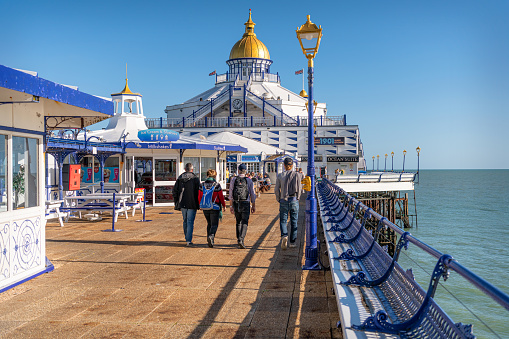 Tourists walking in sunshine on Eastbourne Pier in East Sussex, Eastbourne, England