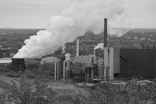 An aerial grayscale shot of an industrial site with smoke coming out of it