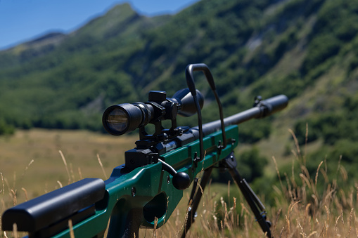 A green military sniper rifle with a scope for long distance tactical modern warfare in yellow grass blue sky.