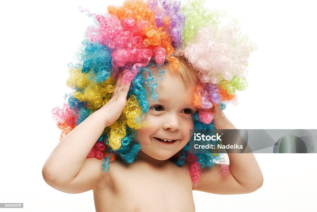 Little boy in colorido brillante wig sonriente sosteniendo la cabeza - Foto de stock de Cabello desmelenado libre de derechos