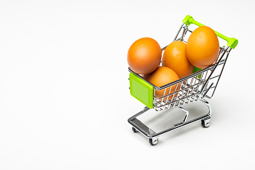 Fresh eggs in a miniature shopping cart as conceptual image.Miniature shopping cart with eggs on white background