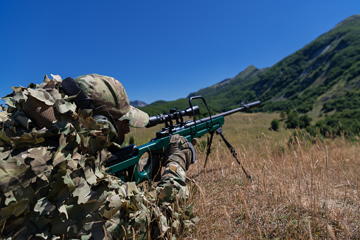 Army soldier holding sniper rifle with scope and aiming in forest. War, army, technology and people concept.