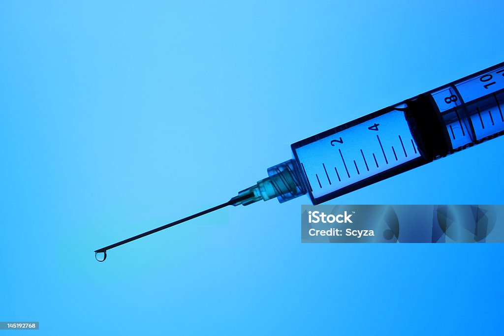 Blue syringe Syringe with a droplet of liquid  on the tip of the needle in front of a blue background. Bacterium Stock Photo