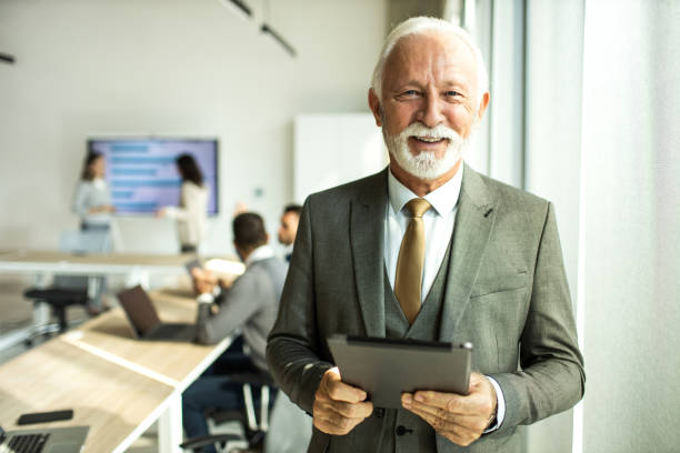 Confident senior man businessman working inside modern office on a digital tablet