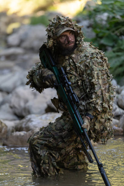 迷彩服を着た軍人またはエアガン奏者が川をこっそりと歩き回り、スナイパーライフルから横または標的を狙う。 - wet spy men suit ストックフォトと画像