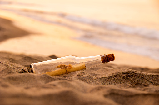 This is a side view close up color photograph of a Message in a Bottle on Sand dune at Sunset