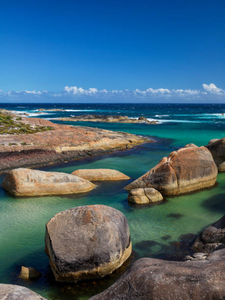 Smooth granite boulders create sheltered ocean swimming hole with blue sky and light clouds