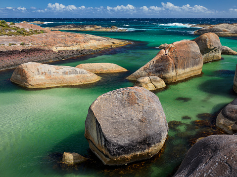 Smooth granite boulders create sheltered ocean swimming hole with blue sky and light clouds