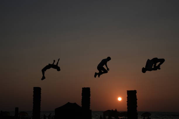 Sunset time on the beach . Three young men having fun leaping over palm trunks! of Gaza City August 19, 2022.