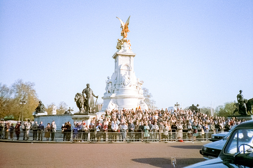 London, England- 1983: A vintage 1980's Nikon negative film scan of crowds of tourists, onlookers and royal guard around The Queen Victoria Memorial in front of Buckingham Palace, in London, England