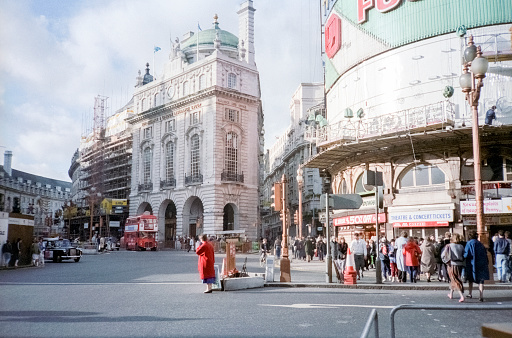 London, England- 1983: A vintage 1980's Nikon negative film scan of the streets and famous intersection of of Piccadilly Circus, London with distinct architectural buildings and cars parked on the road.