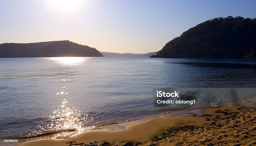 afternoon lake beach hills late afternoon sunlight dazzling reflections on coastal lake landscape with surrounding bushy hills and mountains. beautiful clear blue sky Coastline Stock Photo