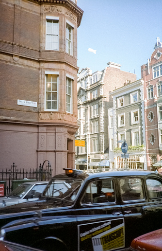 London, England- 1983: A vintage 1980's Nikon negative film scan of the streets of Mayfair, London with distinct architectural buildings and cars parked on the road.