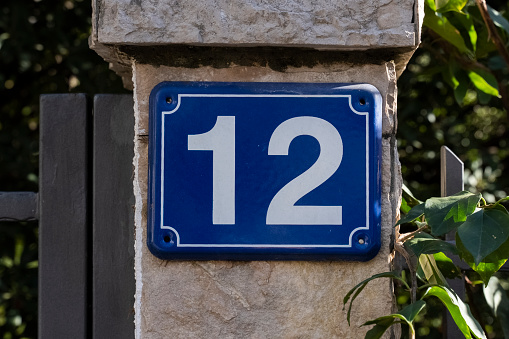 close-up of a rectangular sign signifying the house number with white numbers 12. Signs indicating the address of the house.