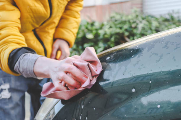 istock A young caucasian guy without a face in a yellow jacket rubs his hands with a pink rag and wipes the headlight 1451997552