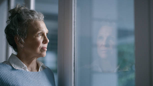 istock Depression, sad and lonely with a senior woman by  a window, standing in her home while thinking of an idea. Glass, mental health and retirement with an elderly female pensioner in her house alone 1452000763