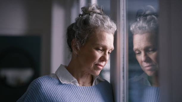 dépression, femme triste et âgée par la fenêtre regardant, bouleversée, seule et malheureuse dans une maison de retraite. santé mentale, solitude et femmes âgées déprimées qui pensent aux problèmes, aux problèmes et aux crises - senior women depression sadness women photos et images de collection