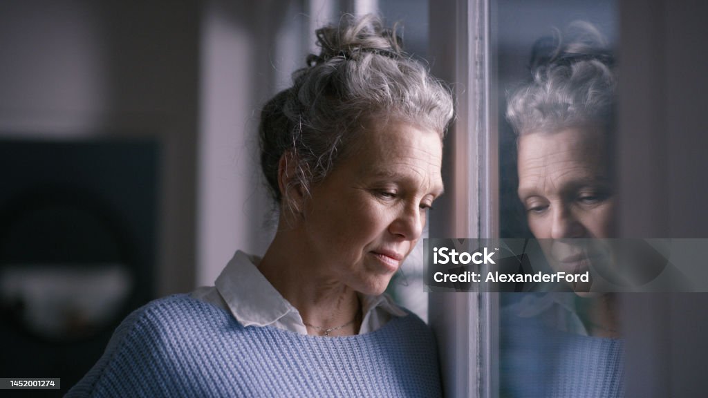 Depression, sad and senior woman by window looking, upset, lonely and unhappy in retirement home. Mental health, loneliness and and depressed elderly female thinking of problem, issues and crisis Sadness Stock Photo