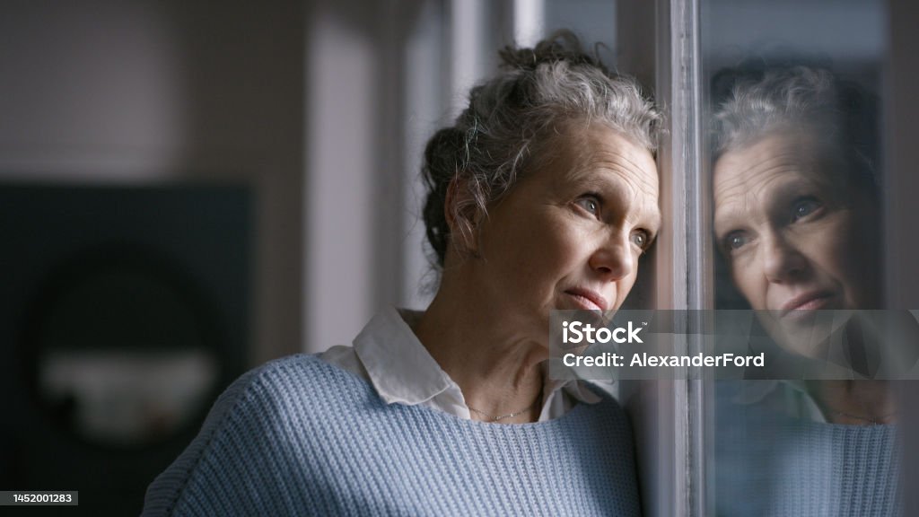 Elderly woman, window reflection and depression while thinking, wonder and mental health in home. Senior lady, retirement anxiety and sad in house with stress, mirror and depressed in San Francisco Depression - Sadness Stock Photo