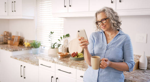 istock Phone, coffee and kitchen with a senior woman browsing social media or typing a text message in her home. Mobile, morning and retirement with a mature female texting or drinking alone in her house 1452014566