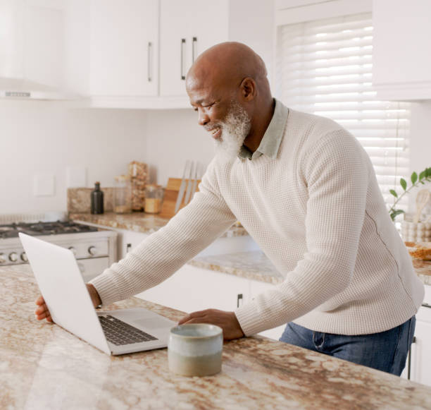 istock Laptop, search and communication with black man in kitchen for email, social media and internet. Contact, online shopping and technology with old man at home for website, insurance or virtual chat 1452016394