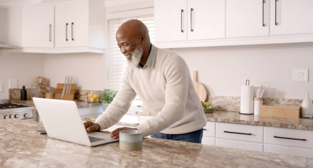 istock Laptop, happiness and senior black man in kitchen working online, using internet and read website content. Technology, communication and elderly male enjoy freedom, holiday and retirement at home 1452016396