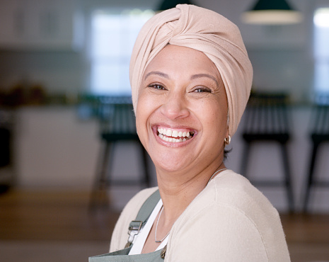 Muslim woman, face or laughing in fashion turban, scarf or traditional head wrap in house or home living room. Portrait, happy smile or mature islamic or makeup cosmetics, trend style or arab clothes