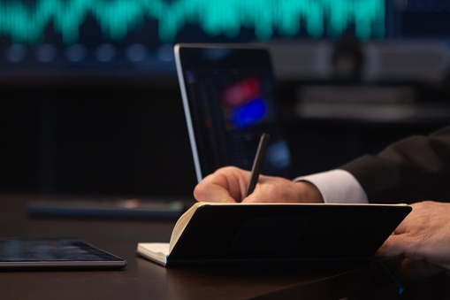 Close-up of male hands writing down information. Financial expert analyzing sales and charts on stock market and making notes with pen in his journal. Market trading, business growth concept
