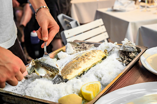 Branzino or Mediterranean sea bass whole roasted in salt fish filleted at the table by a waiter at a street restaurant in Vernazza, Cinque Terre Italy