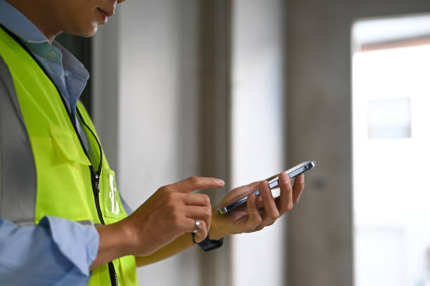istock Cropped shot of engineer man wearing reflective jackets standing in construction site and using smart phone. 1452039495
