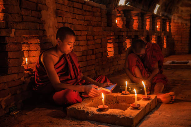 начинающие буддийские монахи, созерцающие внутри храма, мьянма - buddhism monk book zen like стоковые фото и изображения