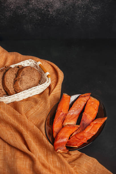 smoked red fish slices on a dark background with bread, minimalism in food