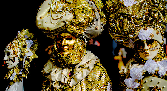 Venice, Italy - February 21, 2022: The Carnival of Venice, when visitors and residents of Venice dress up in wonderfully elaborate costumes and parade through the squares and along the banks of the canals. Here we see once such celebrant in a spectacular gold and green outfit.