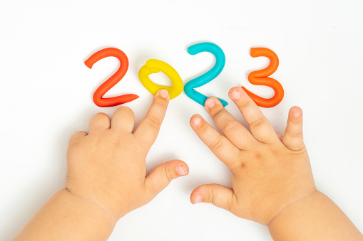 Child's hands playing with figurine 2023 of plasticine on white background. Holiday Art Activity for Kids. Fine motor skills. New Year 2023. Merry christmas concept