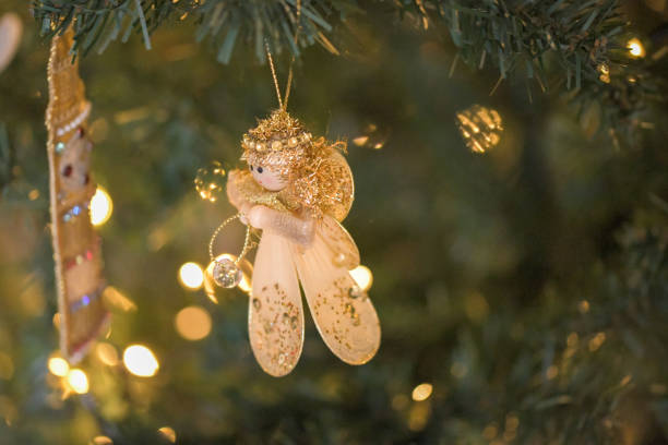 A golden angle hanging decoration surrounded by festive lights hanging from a Christmas tree