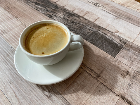 A cup of coffee served in white cup and saucer on a wooden table