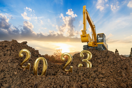 Concept Happy new year 2023,With Crawler excavator lift up bucket in construction site .On Sunset backgrounds