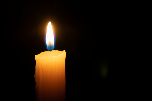 Isolated yellow candle burning on black background. The concept of memory and sorrow.